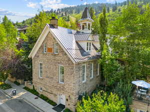 View of side of property featuring an attached garage, a standing seam roof, driveway, stone siding, and a forest view