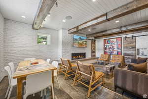 Living area with a barn door, brick wall, beam ceiling, a large fireplace, and recessed lighting