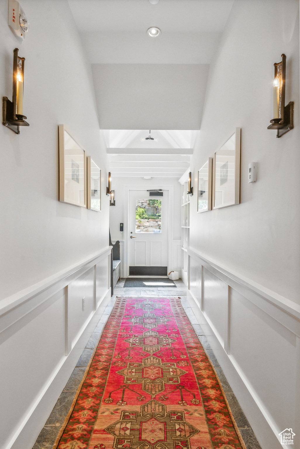 Doorway to outside with a decorative wall, wainscoting, and beamed ceiling