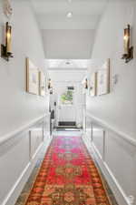 Doorway to outside with a decorative wall, wainscoting, and beamed ceiling