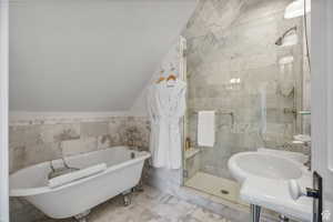 Full bath with tile walls, a shower stall, a soaking tub, marble look tile flooring, and vaulted ceiling