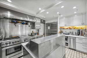 Kitchen featuring high end appliances, backsplash, recessed lighting, white cabinetry, and range hood