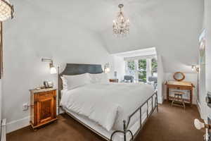 Bedroom with dark colored carpet, a chandelier, and vaulted ceiling
