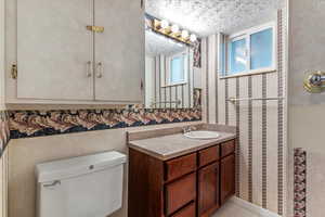 Bathroom featuring vanity, a textured ceiling, tile patterned floors, and wallpapered walls