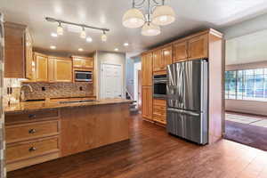 Kitchen with stainless steel appliances, a peninsula, dark stone counters, backsplash, and dark wood-type flooring