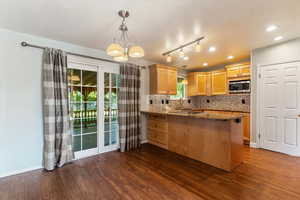Kitchen featuring a peninsula, tasteful backsplash, a chandelier, dark wood finished floors, and dark stone countertops