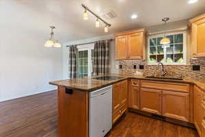 Kitchen featuring a peninsula, white dishwasher, backsplash, dark wood-type flooring, and dark stone countertops