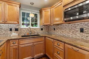 Kitchen with stainless steel microwave, stone countertops, pendant lighting, and decorative backsplash