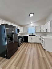 Kitchen with black appliances, a textured ceiling, light countertops, white cabinets, and light wood-style flooring