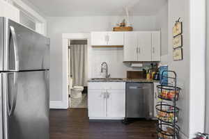 Kitchen featuring appliances with stainless steel finishes, dark stone counters, dark wood-style floors, white cabinets, and tasteful backsplash