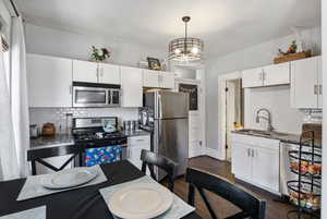 Kitchen featuring decorative backsplash, stainless steel appliances, dark wood finished floors, white cabinetry, and dark stone countertops