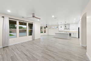 Unfurnished living room with recessed lighting, light wood finished floors, ceiling fan, and arched walkways