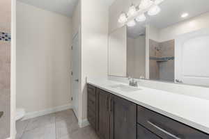 Full bathroom with vanity, tiled shower, and light tile patterned floors