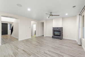 Unfurnished living room with light wood-style flooring, arched walkways, stairway, a stone fireplace, and recessed lighting