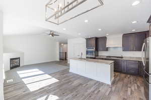 Kitchen featuring dark brown cabinetry, stainless steel appliances, a fireplace, wood finished floors, and open floor plan