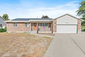 Ranch-style home featuring covered porch, brick siding, roof mounted solar panels, an attached garage, and driveway