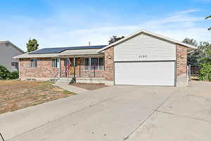 Ranch-style home with brick siding, concrete driveway, solar panels, and a garage