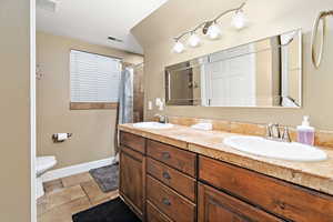 Full bathroom with double vanity, curtained shower, and stone tile floors