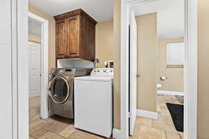 Washroom with stone tile flooring, washer and clothes dryer, and cabinet space