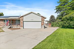 Ranch-style home with driveway, roof mounted solar panels, brick siding, and a garage