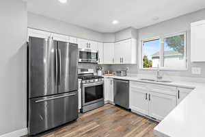 Kitchen with stainless steel appliances, dark wood-style flooring, light countertops, white cabinetry, and recessed lighting