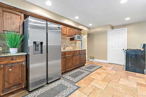 Kitchen featuring stainless steel refrigerator with ice dispenser, recessed lighting, stone tile flooring, gas range, and decorative backsplash