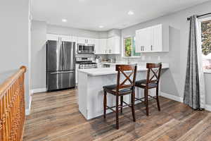 Kitchen featuring appliances with stainless steel finishes, a peninsula, dark wood-type flooring, light countertops, and a kitchen bar