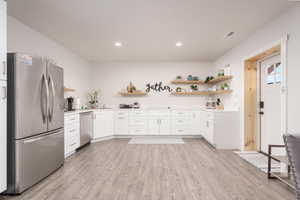 Kitchen featuring open shelves, appliances with stainless steel finishes, light countertops, light wood finished floors, and white cabinets