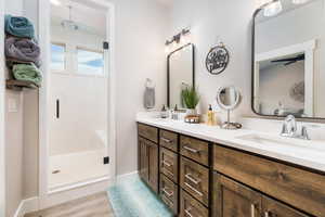 Full bathroom with a shower stall, double vanity, and wood finished floors