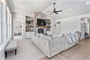 Living room with lofted ceiling, a stone fireplace, ceiling fan, recessed lighting, and light wood finished floors