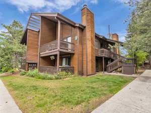 View of side of home with a chimney, a yard, and a balcony