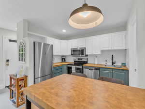 Kitchen with butcher block counters, appliances with stainless steel finishes, white cabinets, decorative backsplash, and recessed lighting