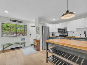 Kitchen featuring butcher block counters, appliances with stainless steel finishes, white cabinets, pendant lighting, and recessed lighting