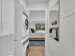 Washroom featuring stacked washing machine and dryer, wood finished floors, and cabinet space