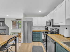 Kitchen featuring wood counters, appliances with stainless steel finishes, light wood finished floors, white cabinetry, and decorative backsplash