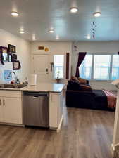 Kitchen with stainless steel dishwasher, a textured ceiling, white cabinetry, light stone counters, and light wood-type flooring