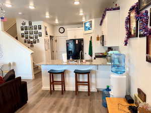 Kitchen featuring a peninsula, black fridge with ice dispenser, white cabinets, light stone counters, and light wood-style floors