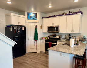 Kitchen featuring stainless steel appliances, a peninsula, light wood-type flooring, a kitchen bar, and light stone countertops