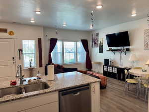 Kitchen with open floor plan, stainless steel dishwasher, light wood-style floors, white cabinets, and light stone counters