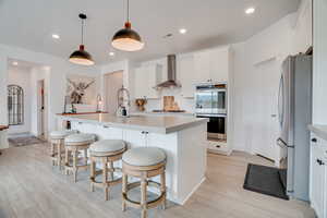 Kitchen with appliances with stainless steel finishes, a center island with sink, a breakfast bar, light wood-type flooring, and light countertops