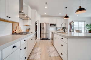 Kitchen featuring light wood-type flooring, decorative backsplash, stainless steel appliances, wall chimney exhaust hood, and recessed lighting