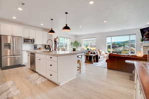 Kitchen with stainless steel appliances, open floor plan, light wood-style floors, recessed lighting, and white cabinets