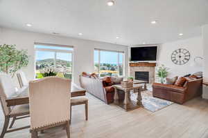 Living area with a stone fireplace, light wood-type flooring, recessed lighting, and a textured ceiling