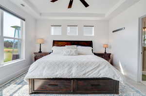 Bedroom featuring a raised ceiling, multiple windows, and ceiling fan