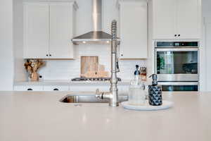 Kitchen featuring tasteful backsplash, light countertops, wall chimney exhaust hood, and double oven