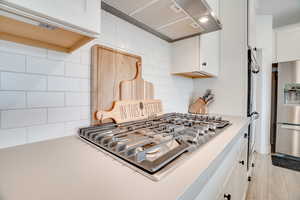Kitchen with appliances with stainless steel finishes, backsplash, wall chimney exhaust hood, and white cabinetry