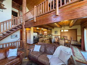 Living area with dark wood-style flooring, a wood ceiling with exposed beams, a chandelier, stairs, and a towering ceiling