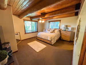Bedroom featuring multiple windows, dark carpet, and a wooden ceiling with exposed beams