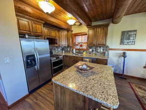 Kitchen with appliances with stainless steel finishes, a wood ceiling with exposed beams, backsplash, dark wood-style flooring, and light stone countertops