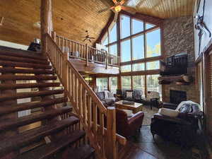 Living room featuring high vaulted ceiling, a stone fireplace, wood ceiling, a ceiling fan, and wood finished floors